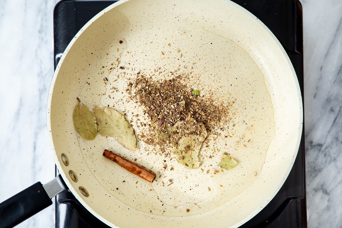 a frying pan with hot oil with added whole spices for making tempering