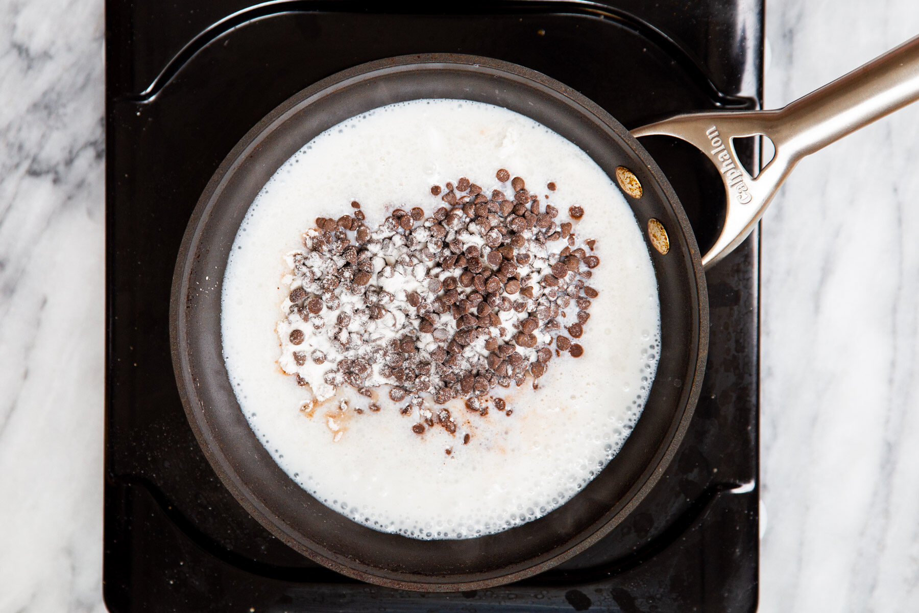 chocolate chips being added to hot coconut milk in a pot