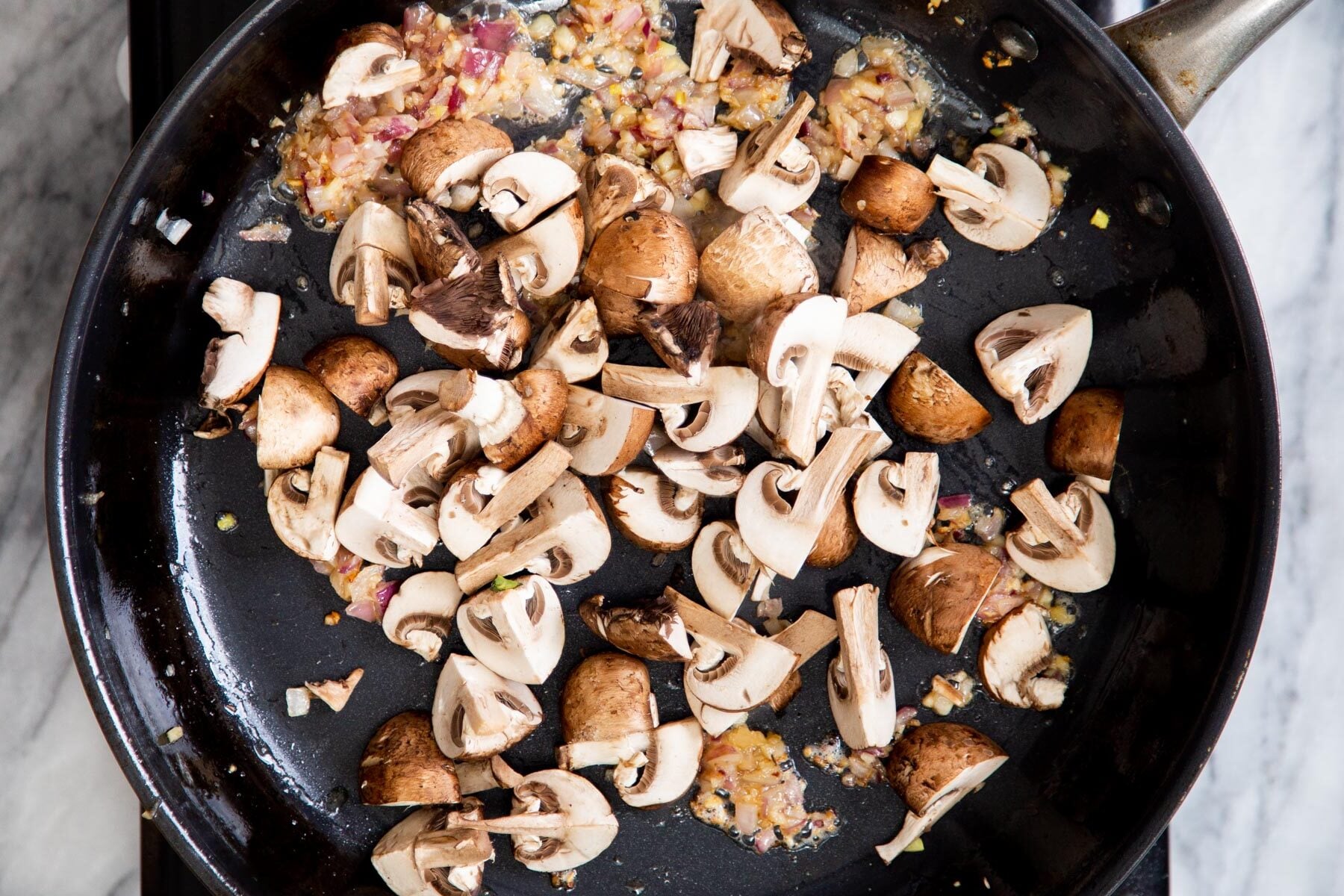 mushrooms being added to sauteed garlic and onion in a skillet