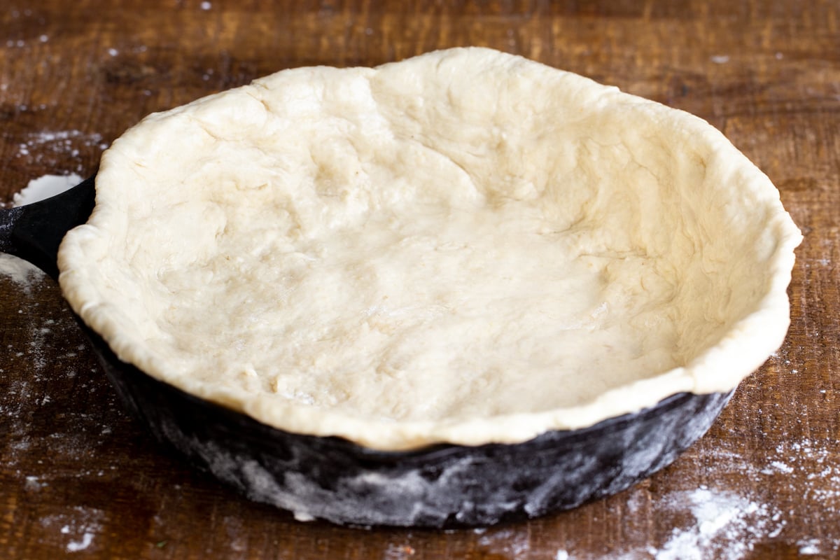 a black cast iron skillet being lined with pretzel pizza crust dough