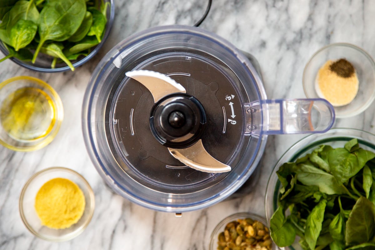 a clean food processor and pesto ingredients on a marble countertop