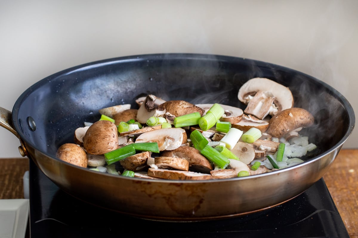 onions, mushrooms and green onions sauteeing in a black skillet