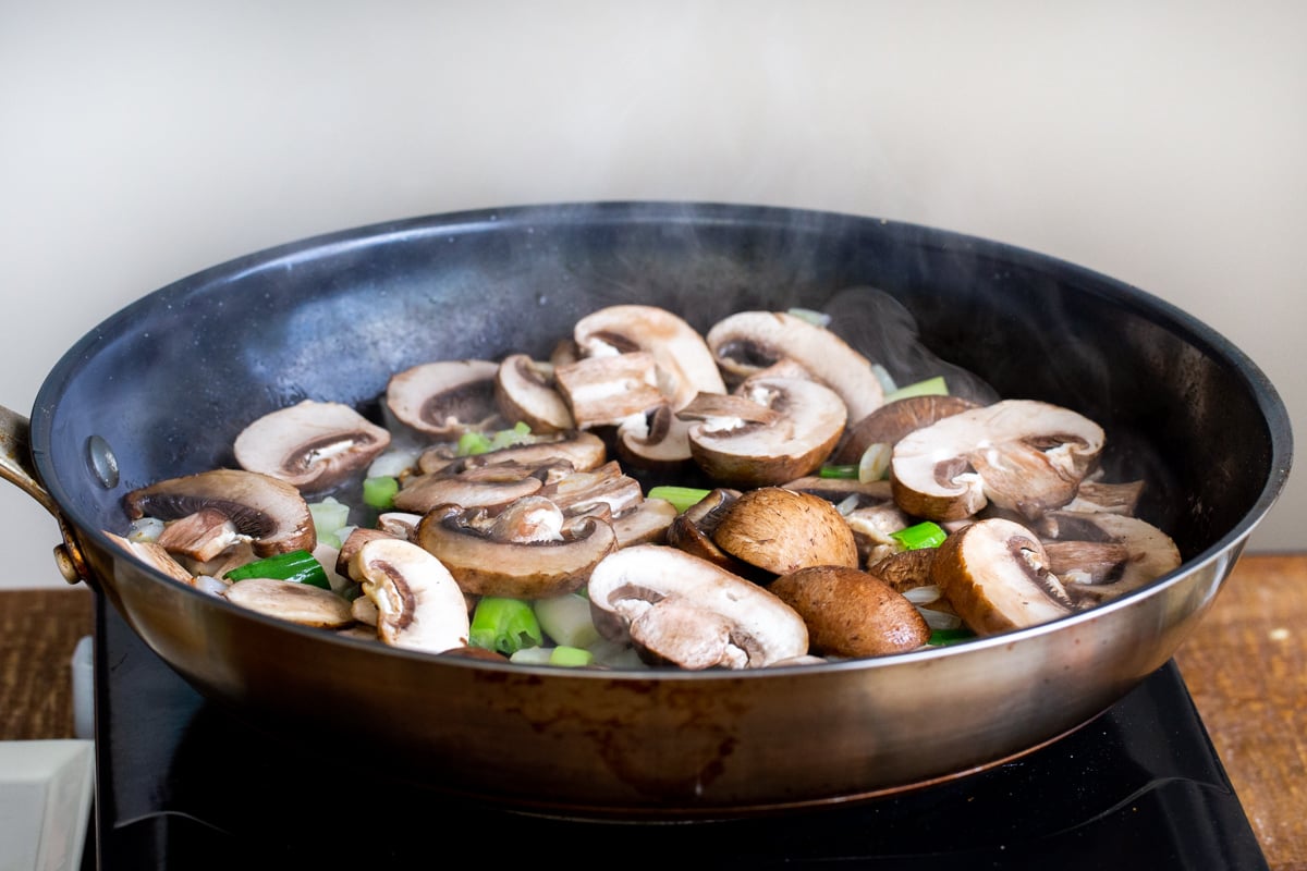 sliced mushrooms and green onions in a black skillet