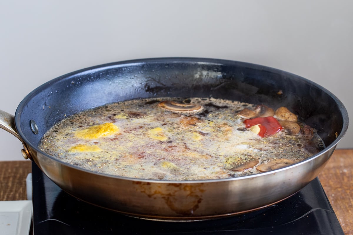 mushrooms simmering in broth in a dark skillet