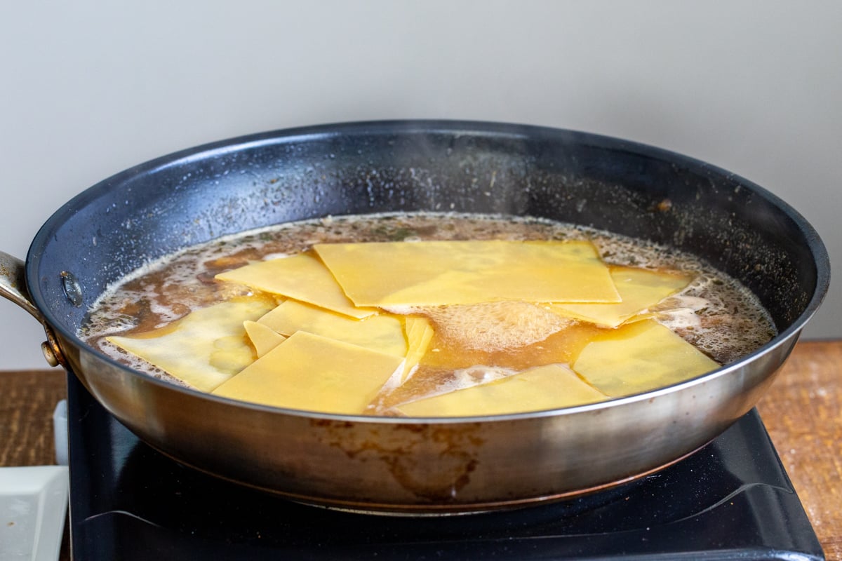 broken lasagna noodles being added to mushroom broth to make skillet lasagna