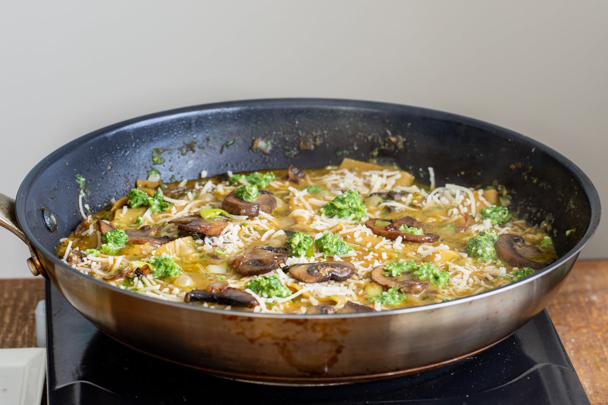 fried mushrooms and basil pesto being added to a black skillet with cooked lasagna noodles