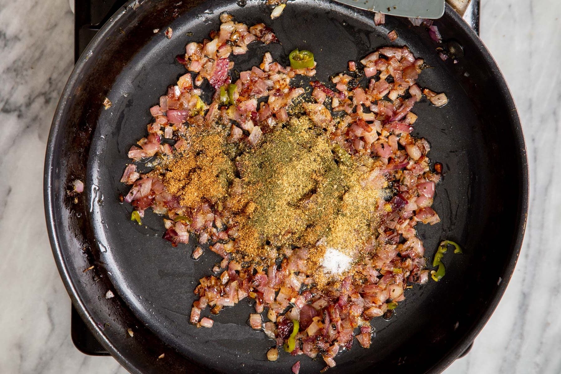 ground spices and minced onions in a black frying pan