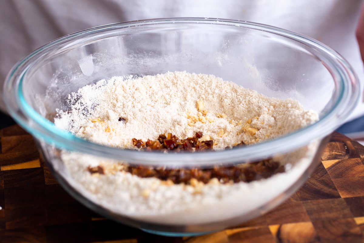 chopped dates and nuts being added to dry cookie ingredients in glass bowl