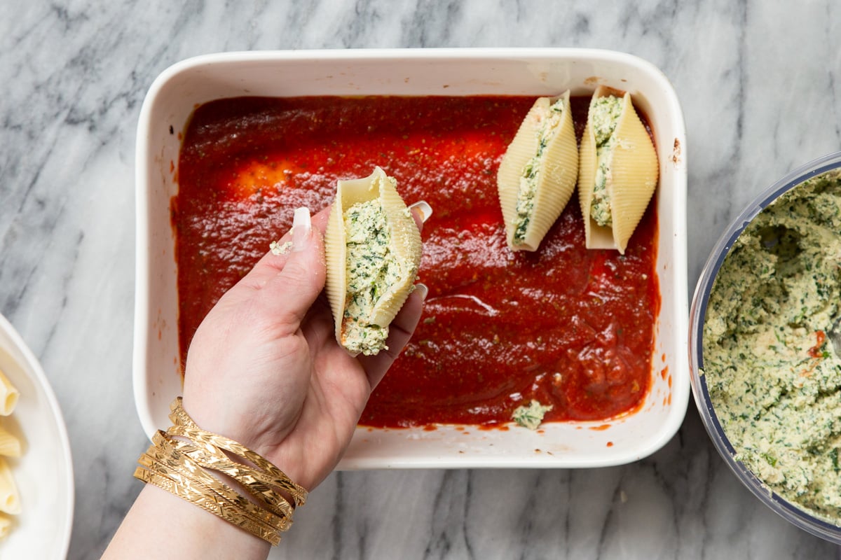 stuffed shells being placed in a casserole dish with marinara sauce 