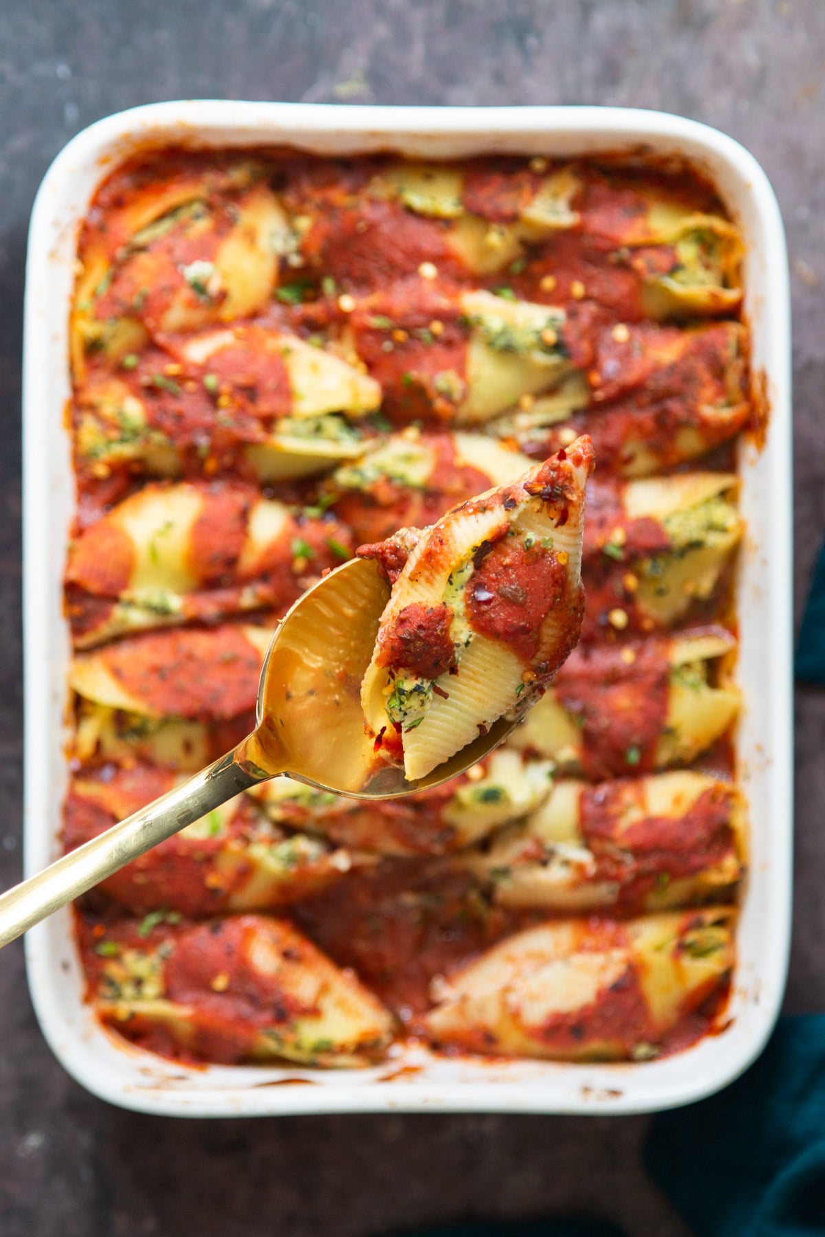 a spoon with a vegan stuffed shell being held over a casserole dish