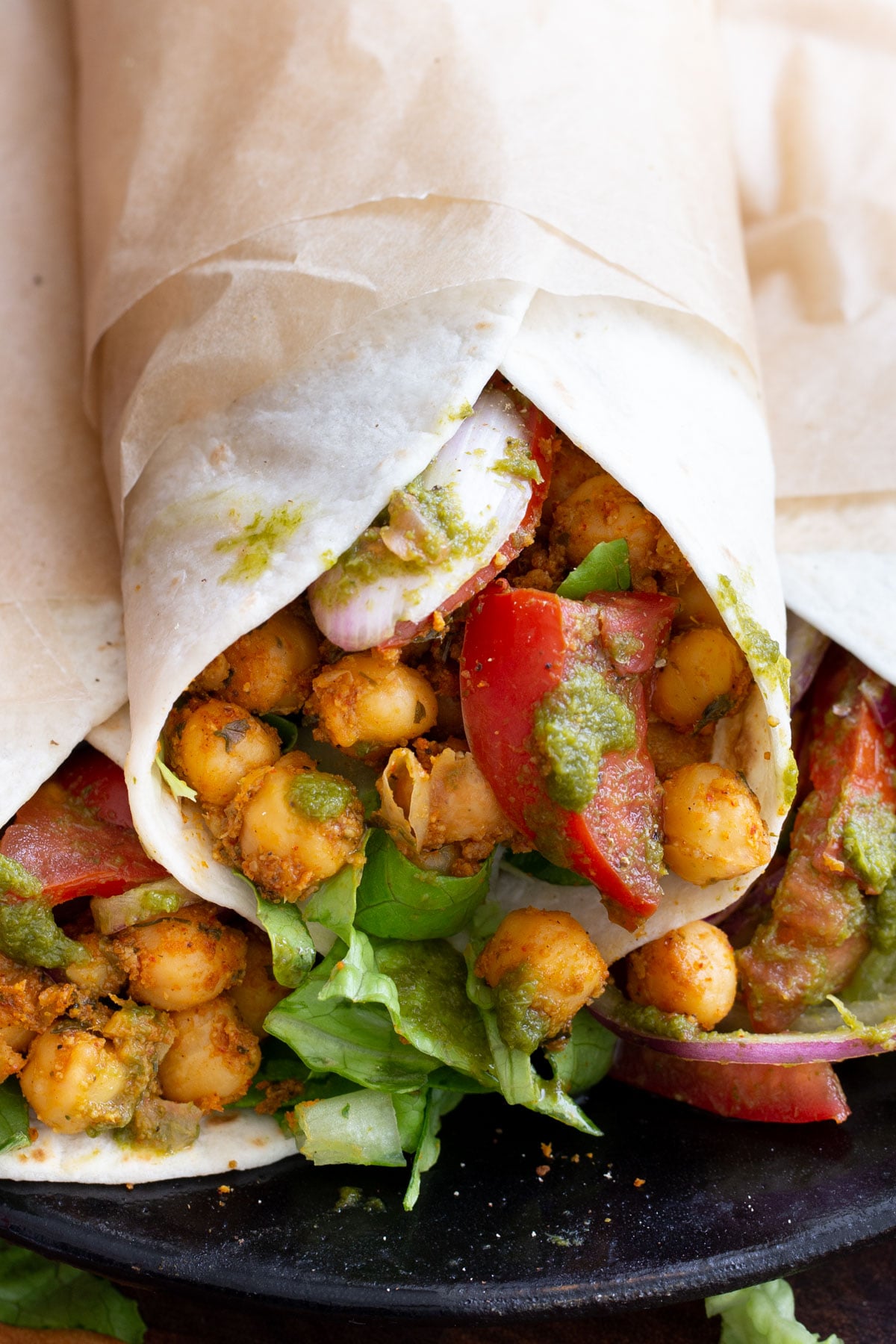 close-up of three chickpea kathi rolls with chutney, tomatoes and onions 