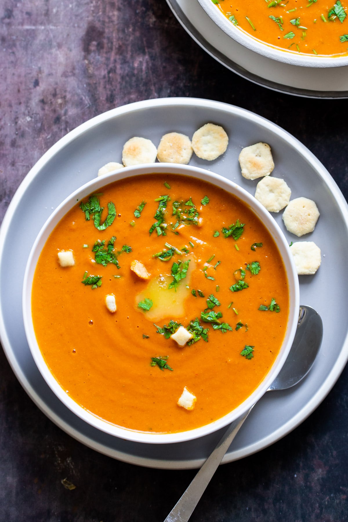 a bowl of vegan roasted tomato soup served on a pale blue plate with small crackers on the side