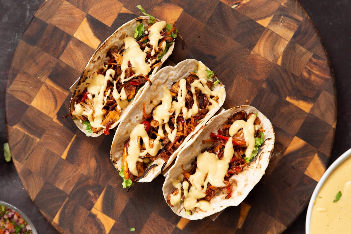 three fully assembled vegan jackfruit tacos on a wooden board
