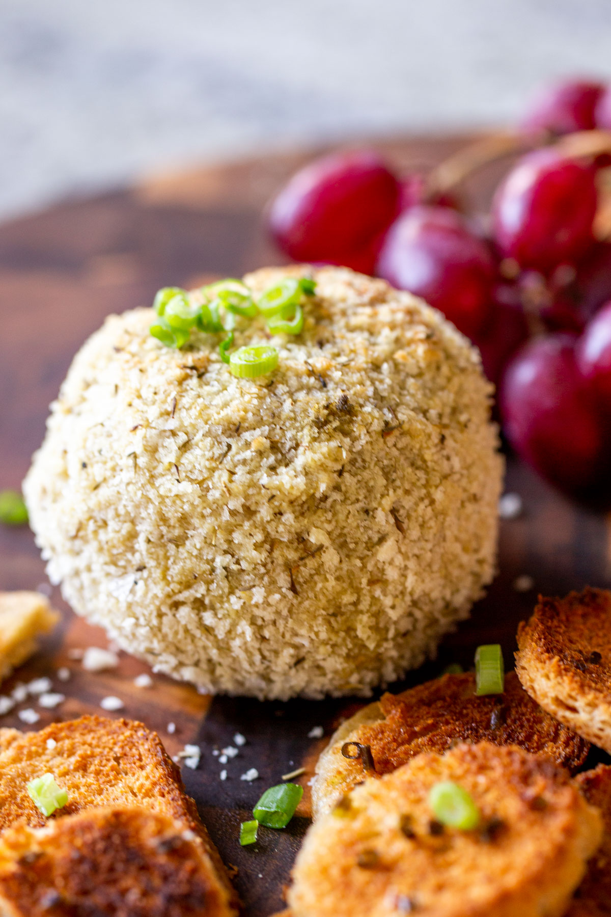 side view of a vegan cheese board with crackers on the side and some grapes in the background