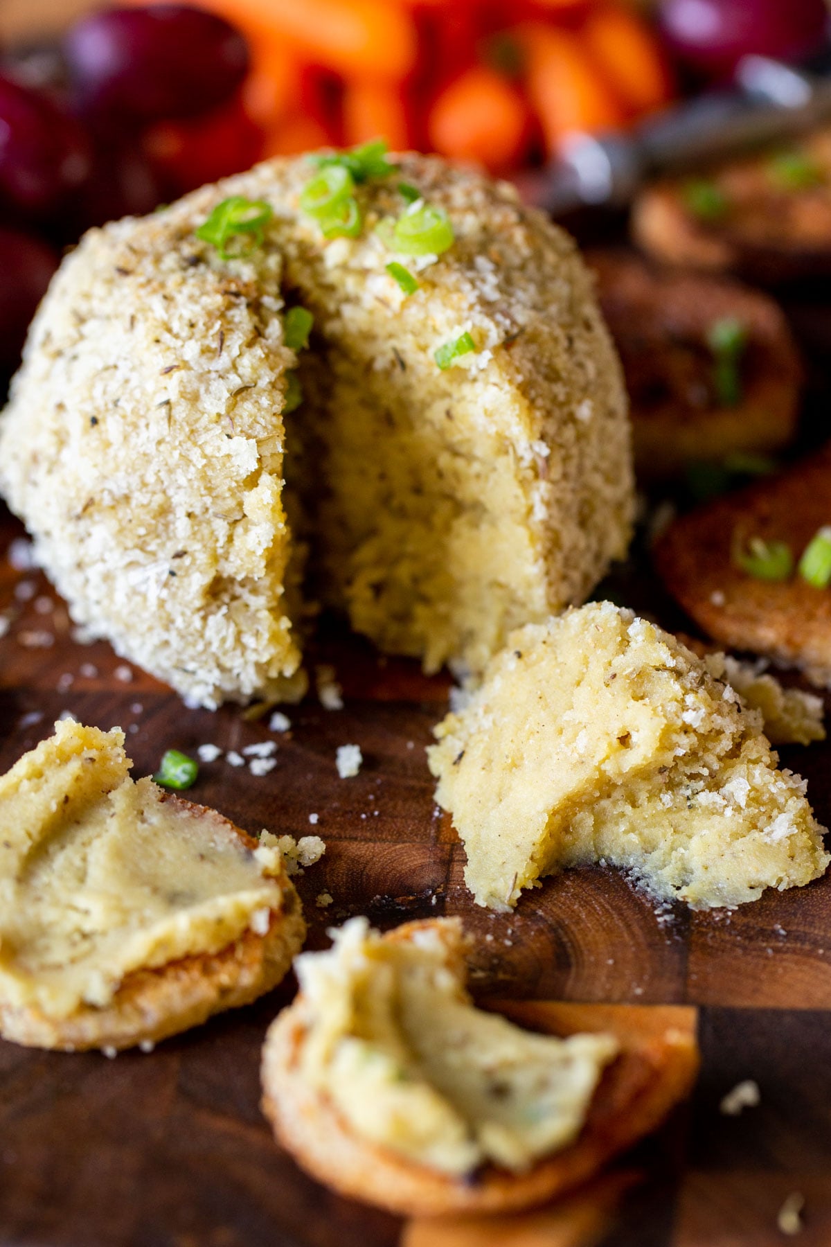 a vegan stuffing flavored cheeseball on a wooden board with one wedge cut