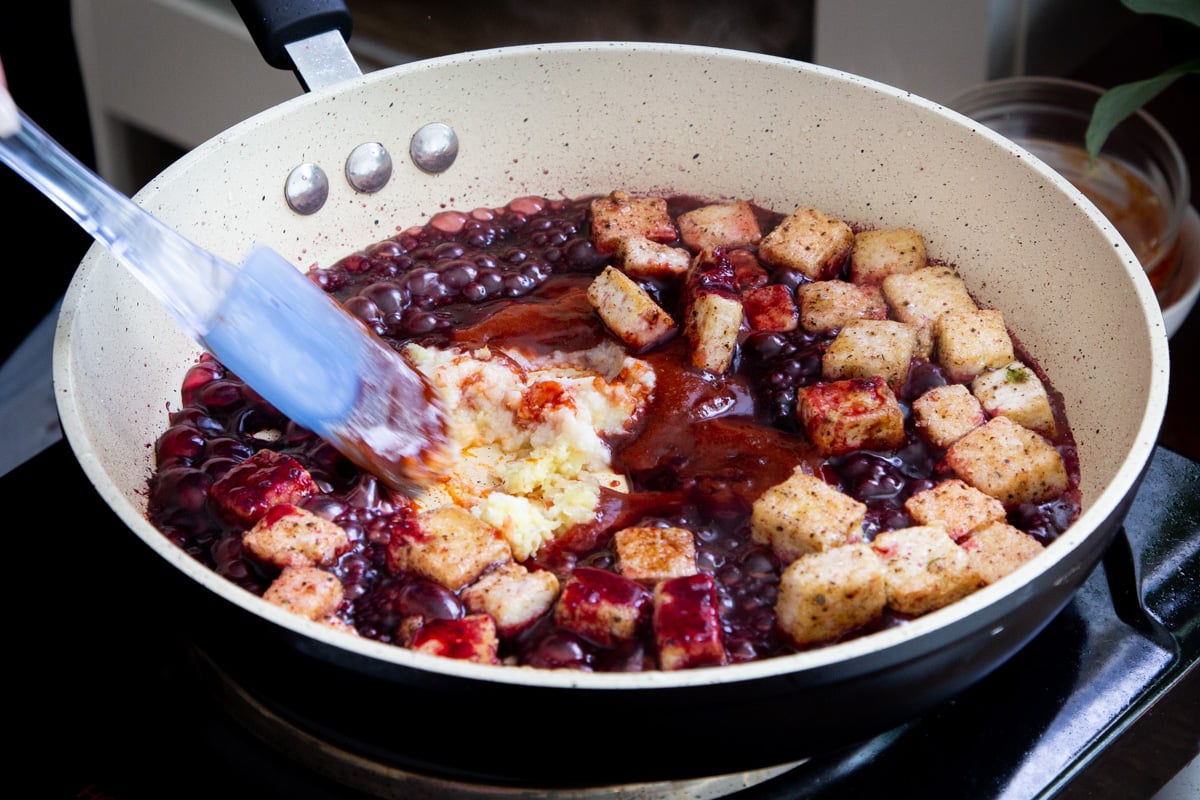 fried tofu cubes being coated in blackberry sauce in a pan