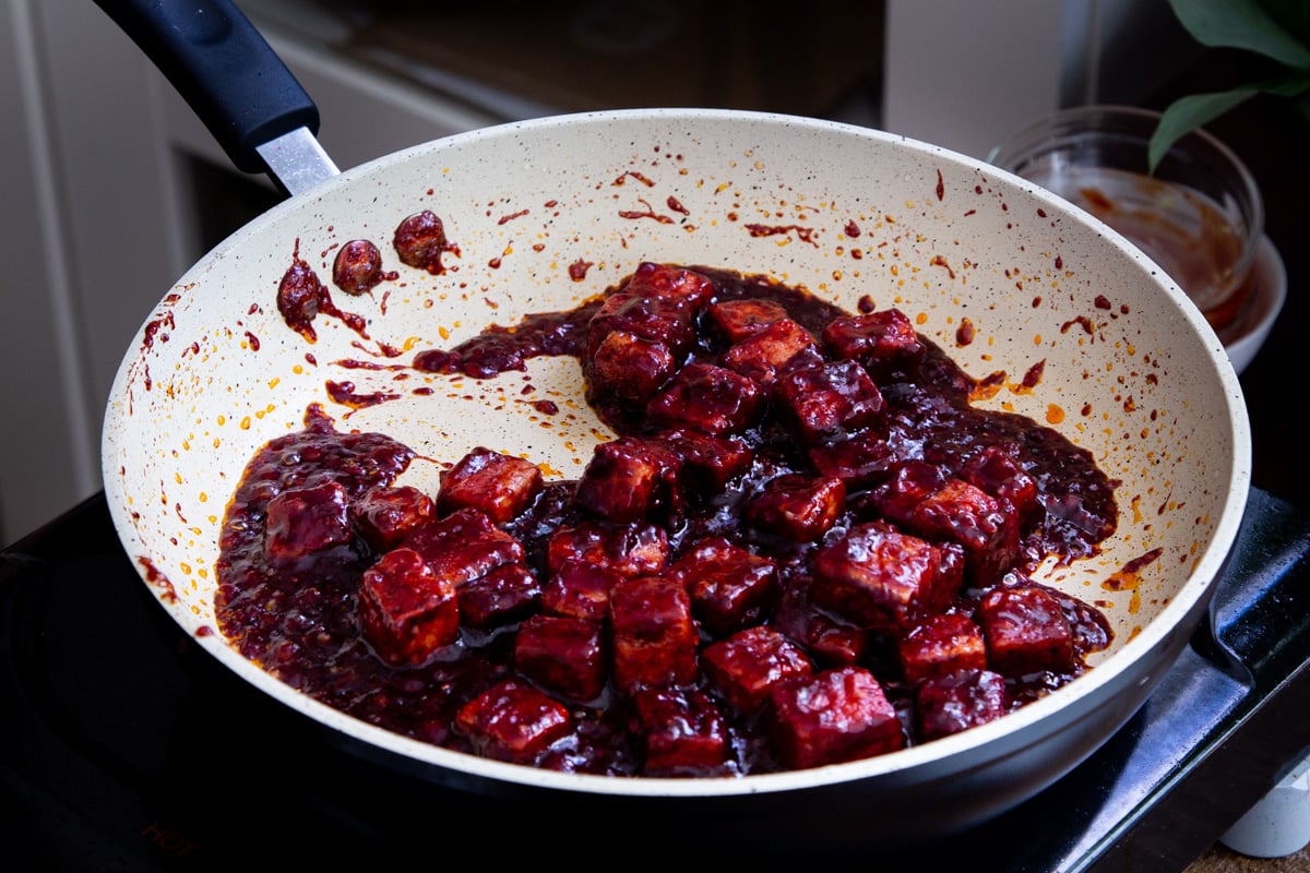 tofu cubes being coated in blackberry sauce in a pan