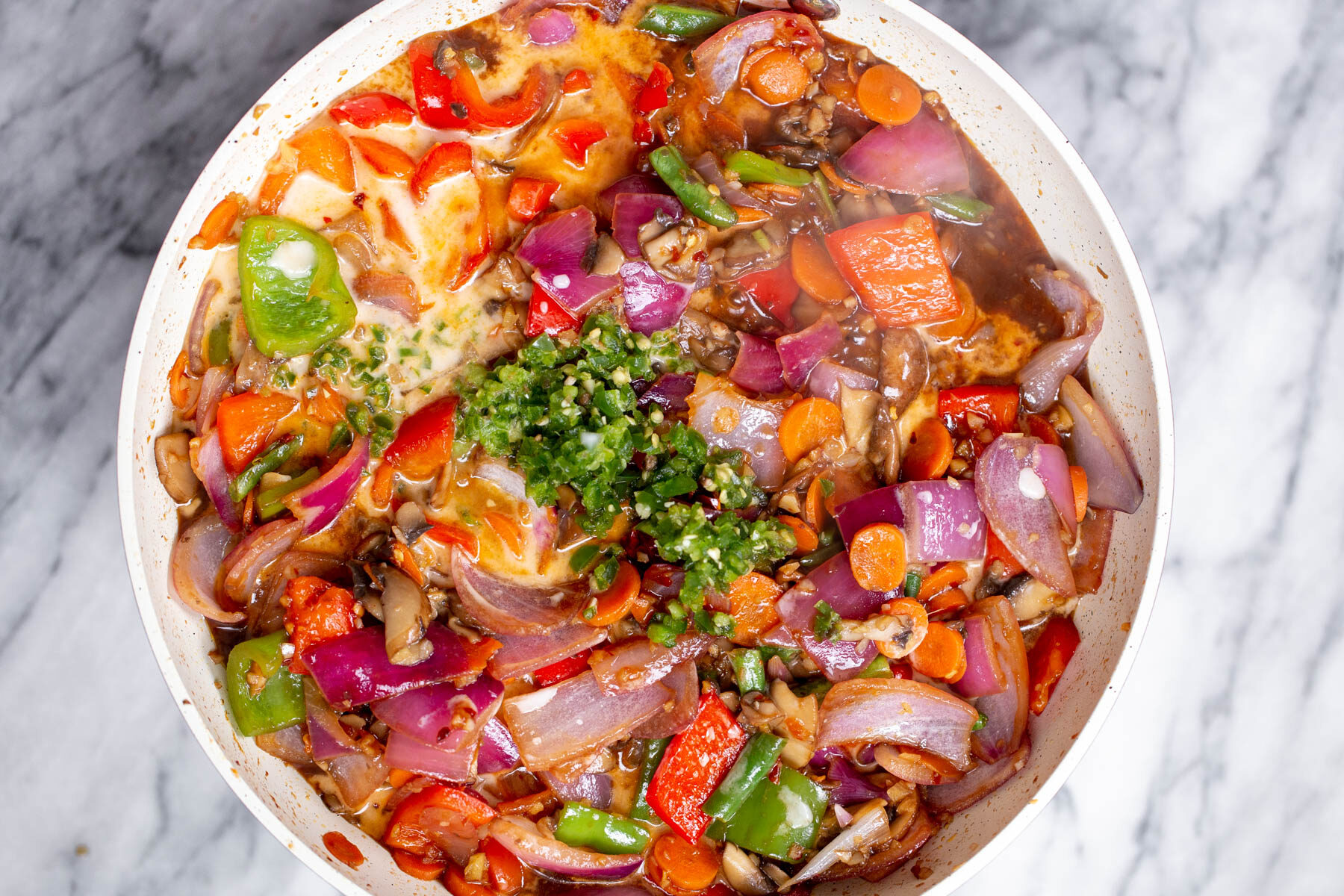 minced green chili being added to a saucepan with vegetables and sweet and sour sauce