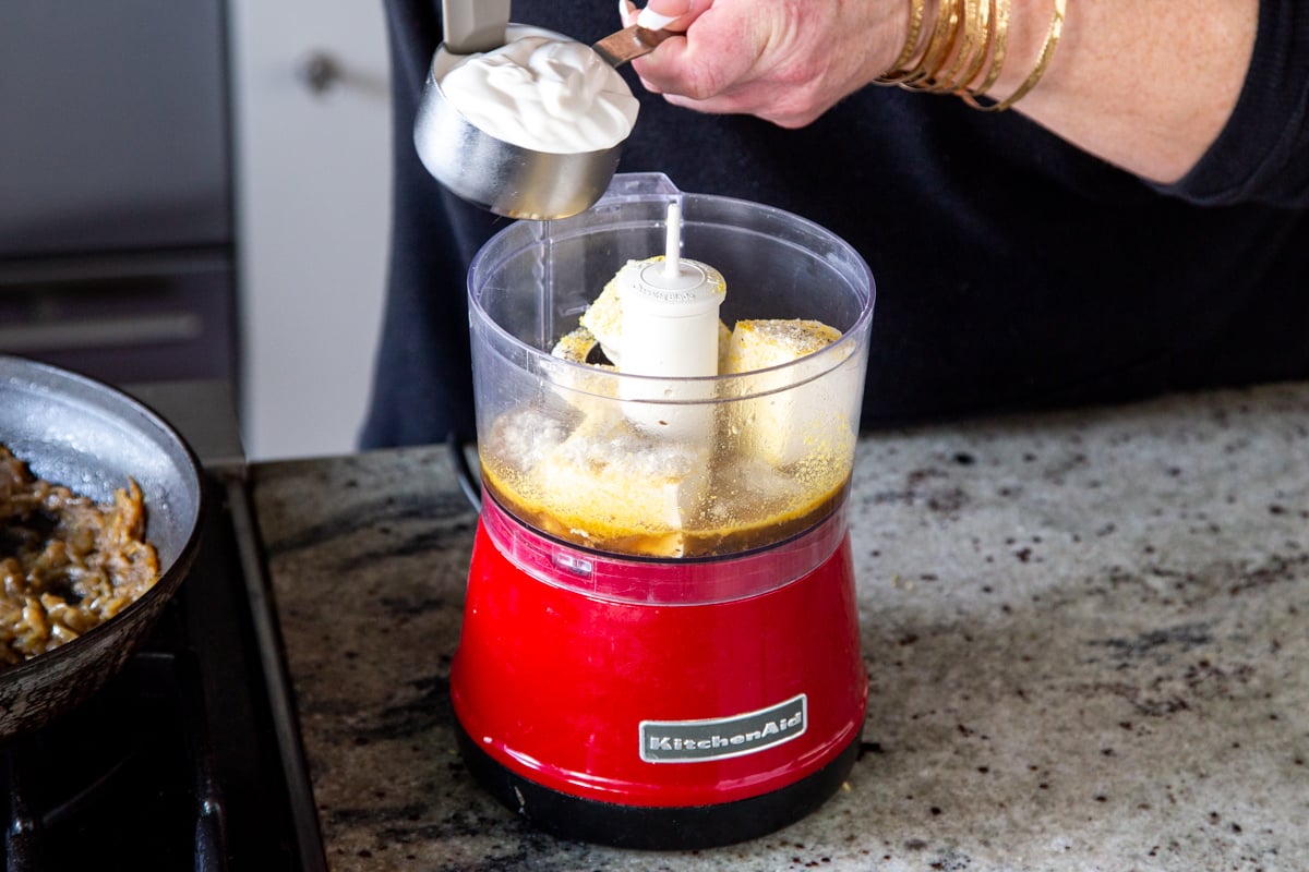 dairy-free yogurt being added to a small food processor with silken tofu and nutritional yeast