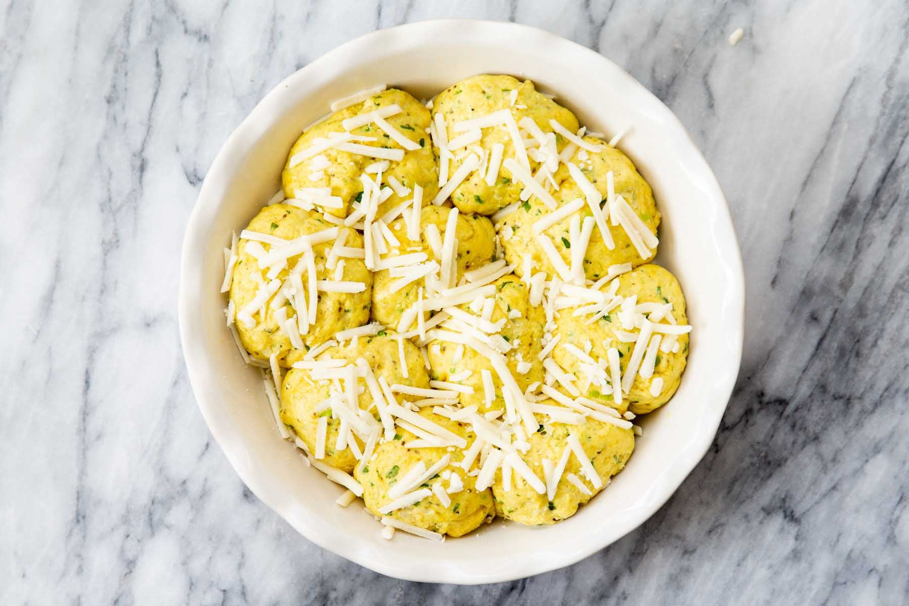 dough balls arranged in a baking dish before baking, cheese added on top