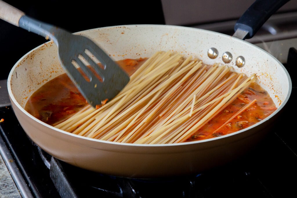 spatula adding dry spaghetti to the pan of sauce