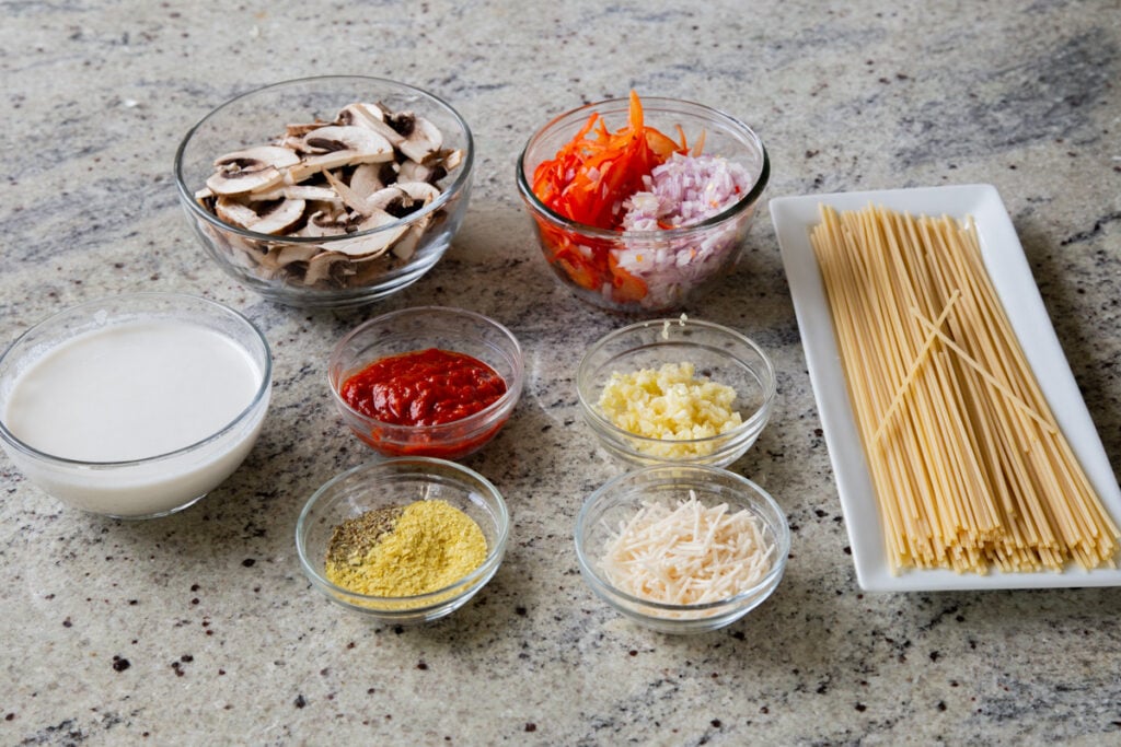 pasta, harissa paste, and other ingredients in bowls on a kitchen countertop