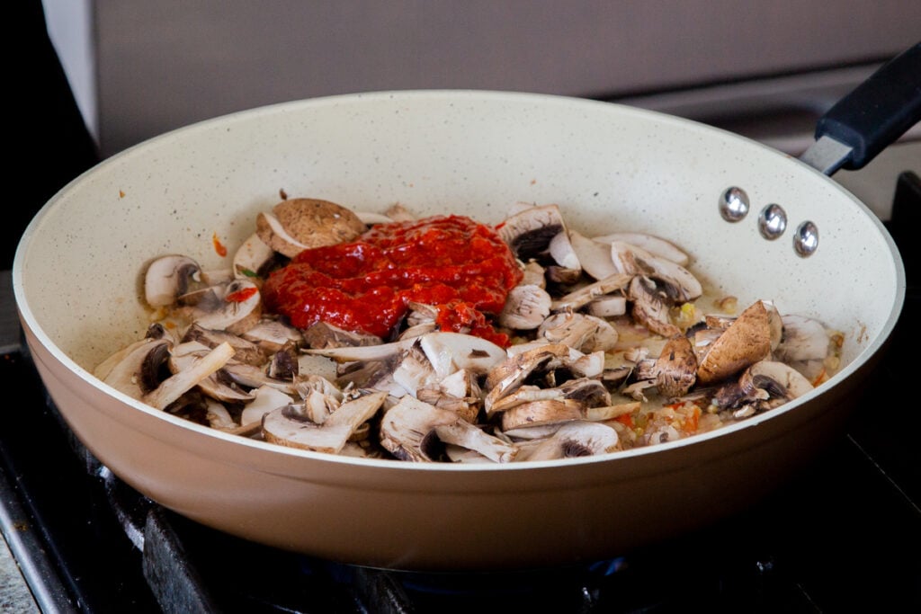 adding mushrooms and harissa paste to the pan