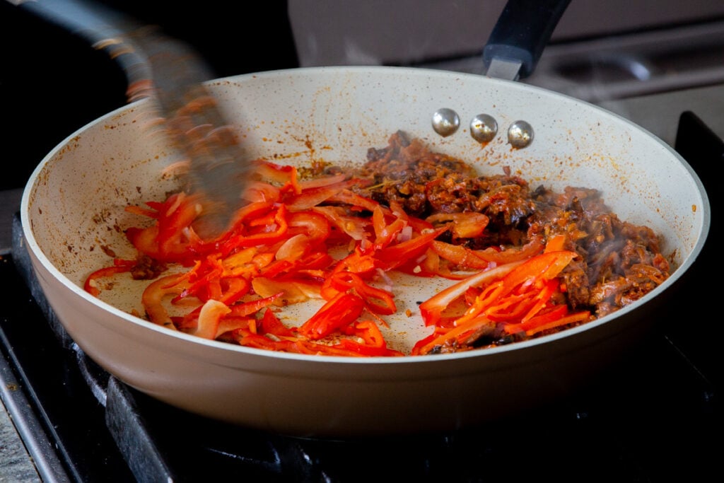 spatula adding sliced bell peppers to the pan