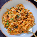 fork taking a bite of harissa pasta with mushrooms and bell pepper in a white bowl