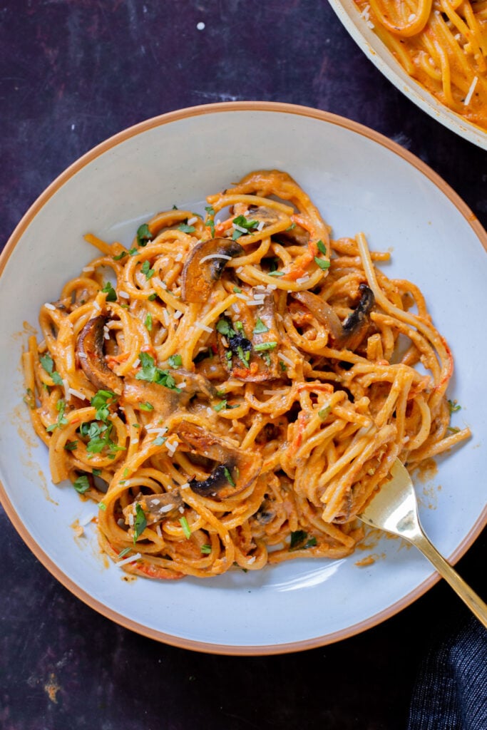 fork taking a bite of harissa pasta with mushrooms and bell pepper in a white bowl
