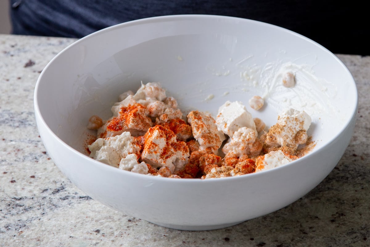 torn tofu and chickpeas in a bowl with non-dairy cream and spices added, before mixing