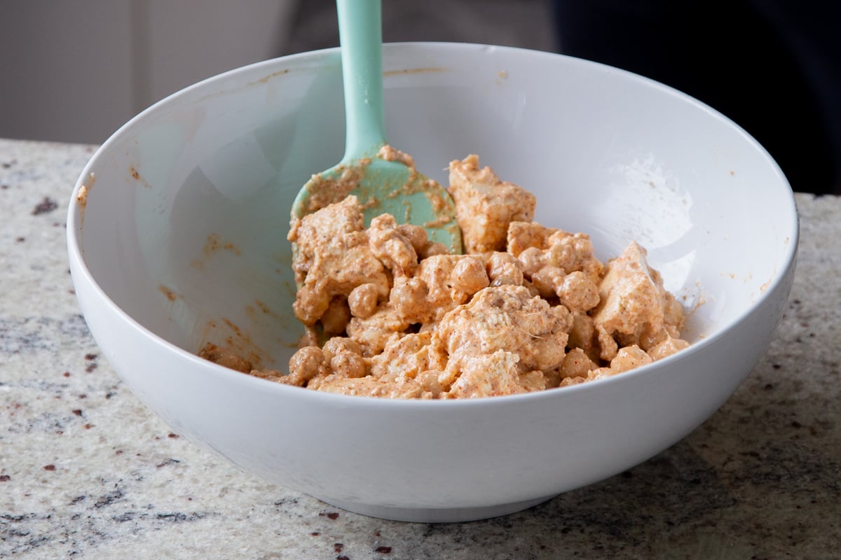 torn tofu and chickpeas in a bowl with non-dairy cream and spices added, after mixing