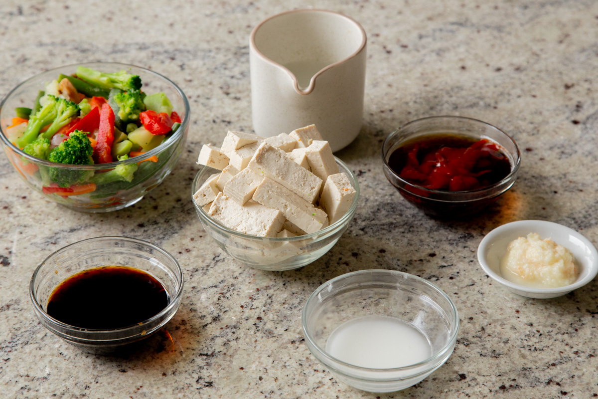 tofu and other stir fry ingredients in bowls on a kitchen counter