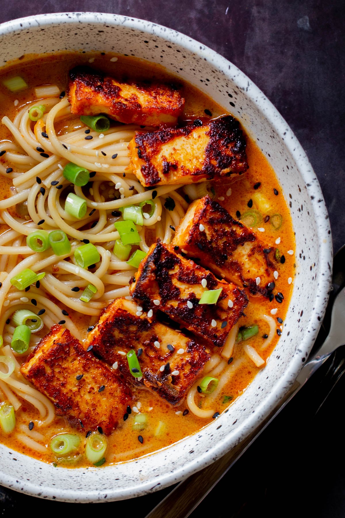 spicy peanut butter ramen in the bowl, after adding tofu, green onions, and sesame seeds