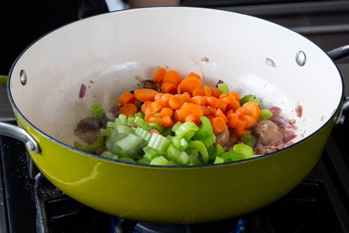 adding veggies to the pan of cooked mushrooms
