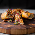 crispy tofu burrito on a wooden cutting board, cut in half so you can see the filling