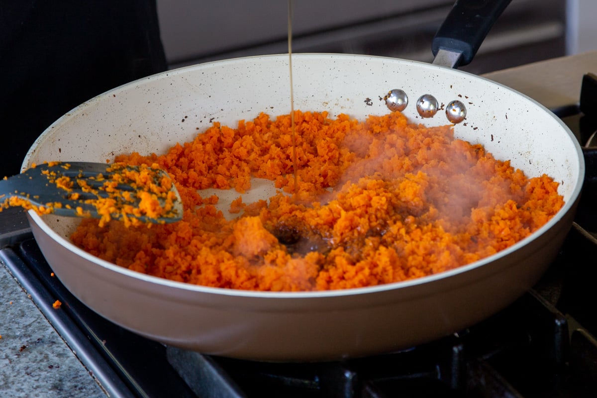 adding maple syrup to the pan of grated carrots