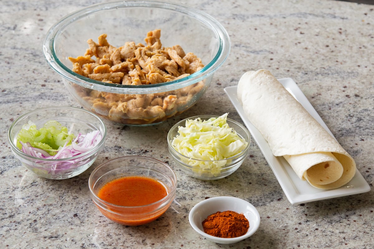 soy curls, buffalo sauce, cajun spice, tortillas, and veggies in bowls on a kitchen counter