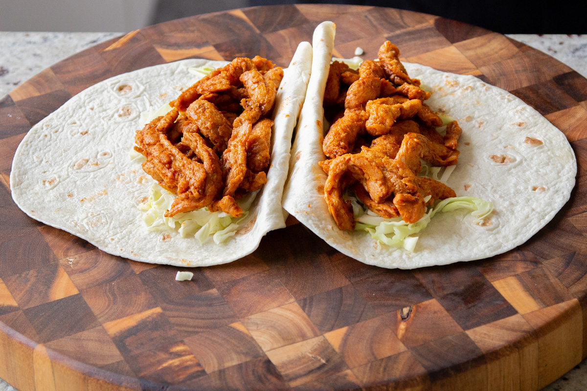 adding the buffalo cajun soy curls on top of the lettuce in the tortillas