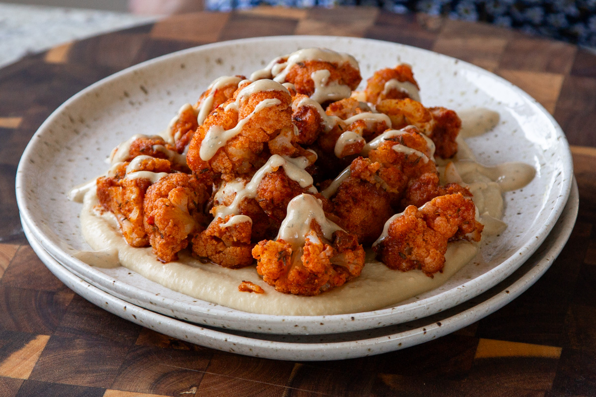 harissa cauliflower on a plate with hummus, and fresh herbs.
