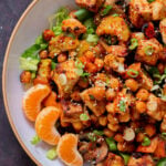 close-up of gochujang tofu and veggies in bowl over lettuce with orange pieces and sesame seeds