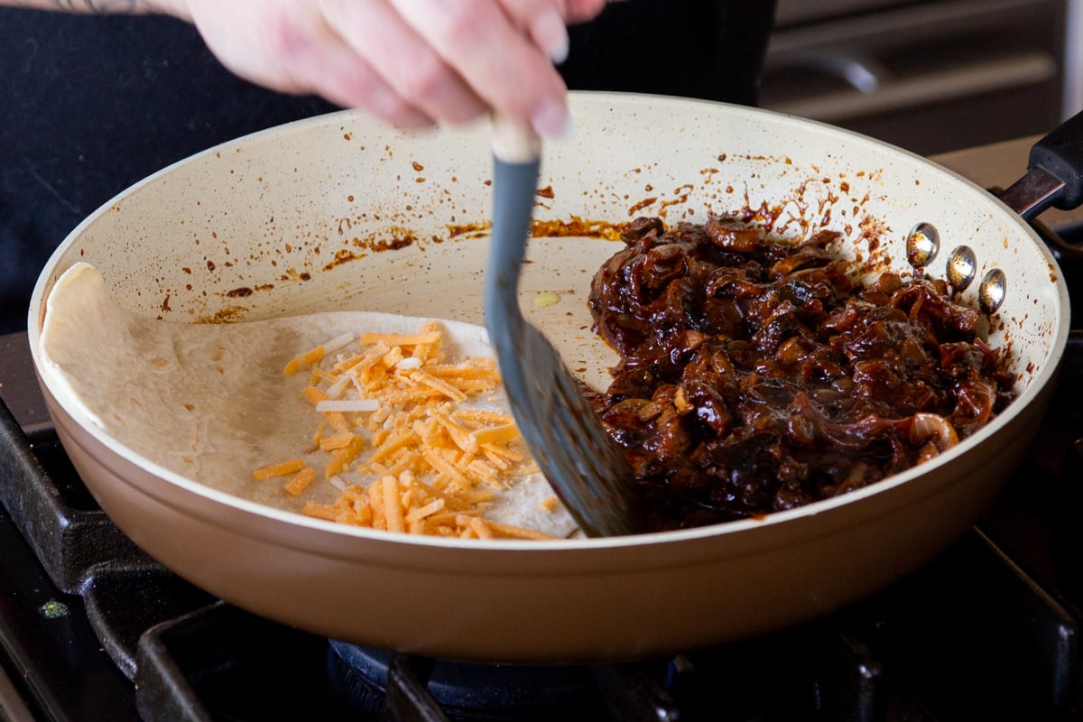 adding cheese to the tortilla in the pan with the mushrooms