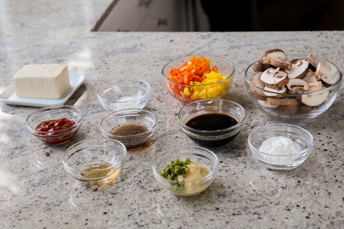 mushrooms, tofu, and other baked stir fry ingredients in bowls on a kitchen counter