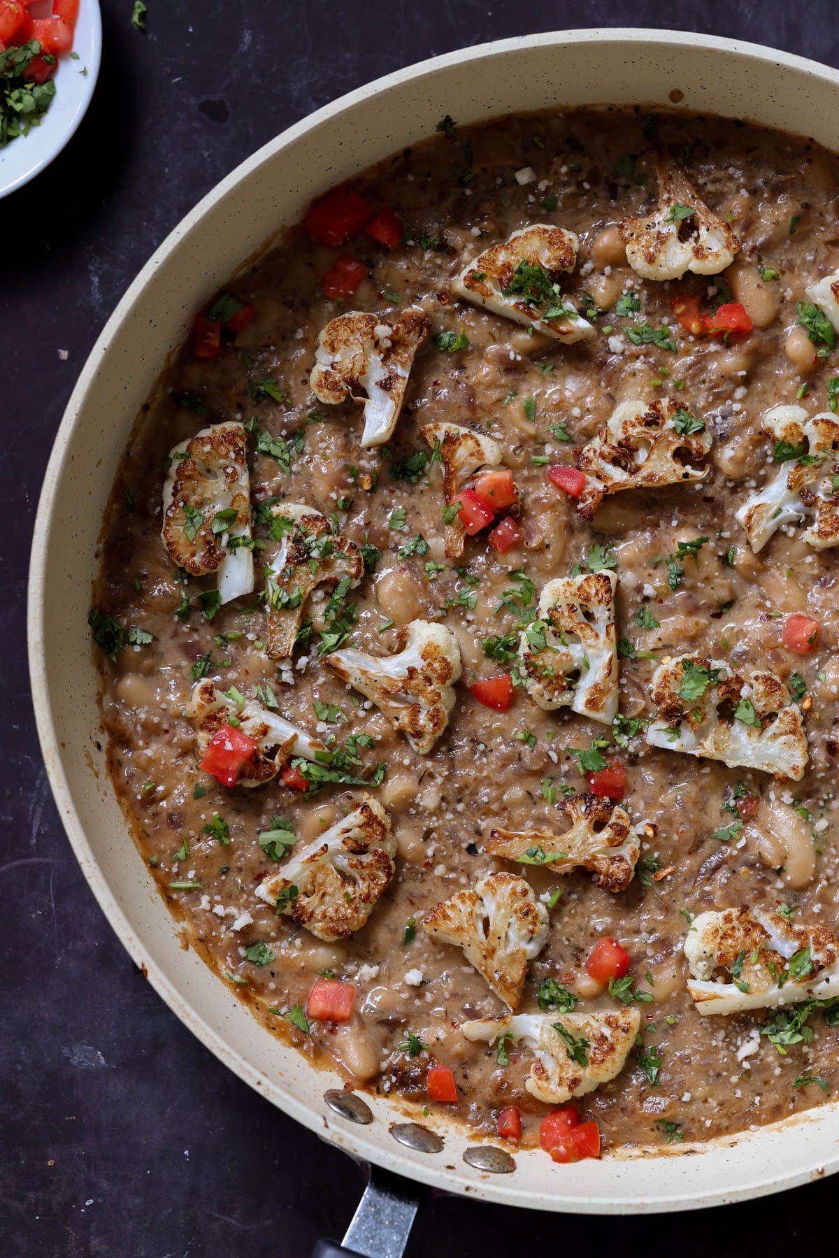 caramelized onion beans in the pan topped with charred cauliflower, tomato, and herbs