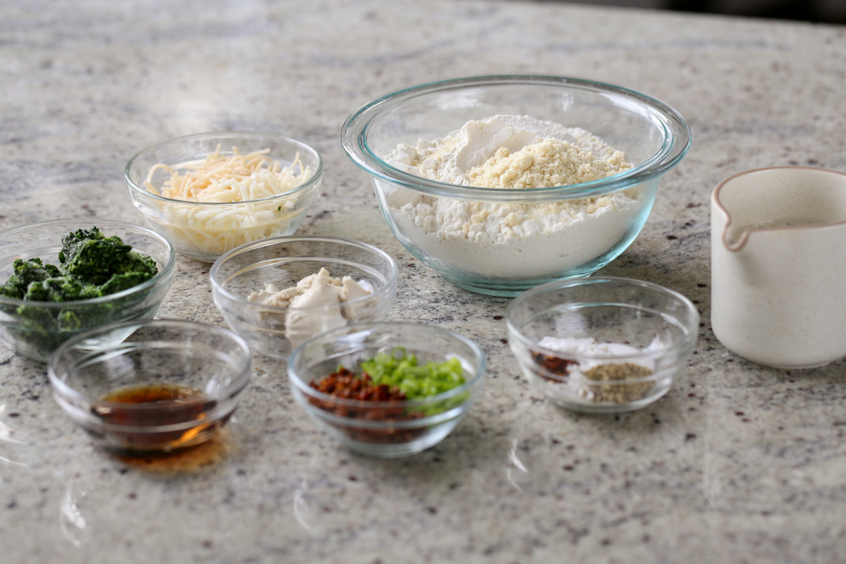 flour, spinach, cheese, and other scones ingredients in bowls on the kitchen counter