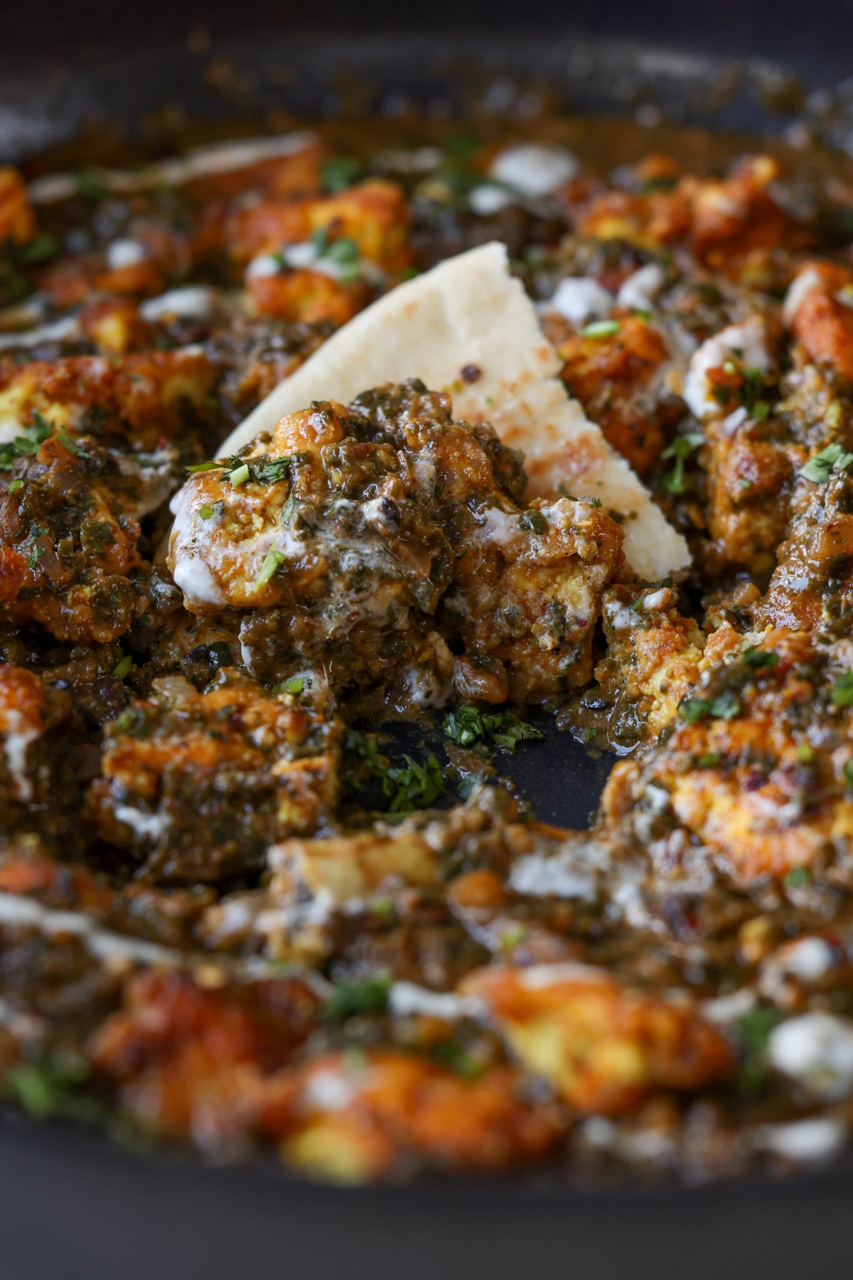 close-up of a piece of flatbread in the pan of chicken saagwala