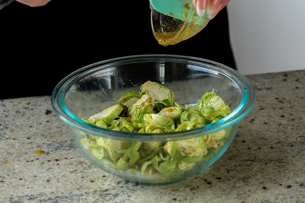 pouring seasonings onto shaved Brussels sprouts in a bowl