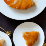 slices of peach upside-down cake on plates next to the cake on a cake stand