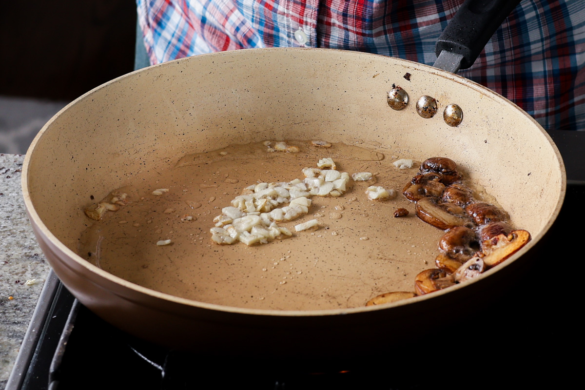 adding garlic to the pan after pushing mushrooms to the side
