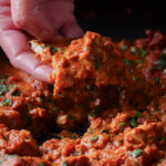 hand scooping up chicken angara with a piece of naan